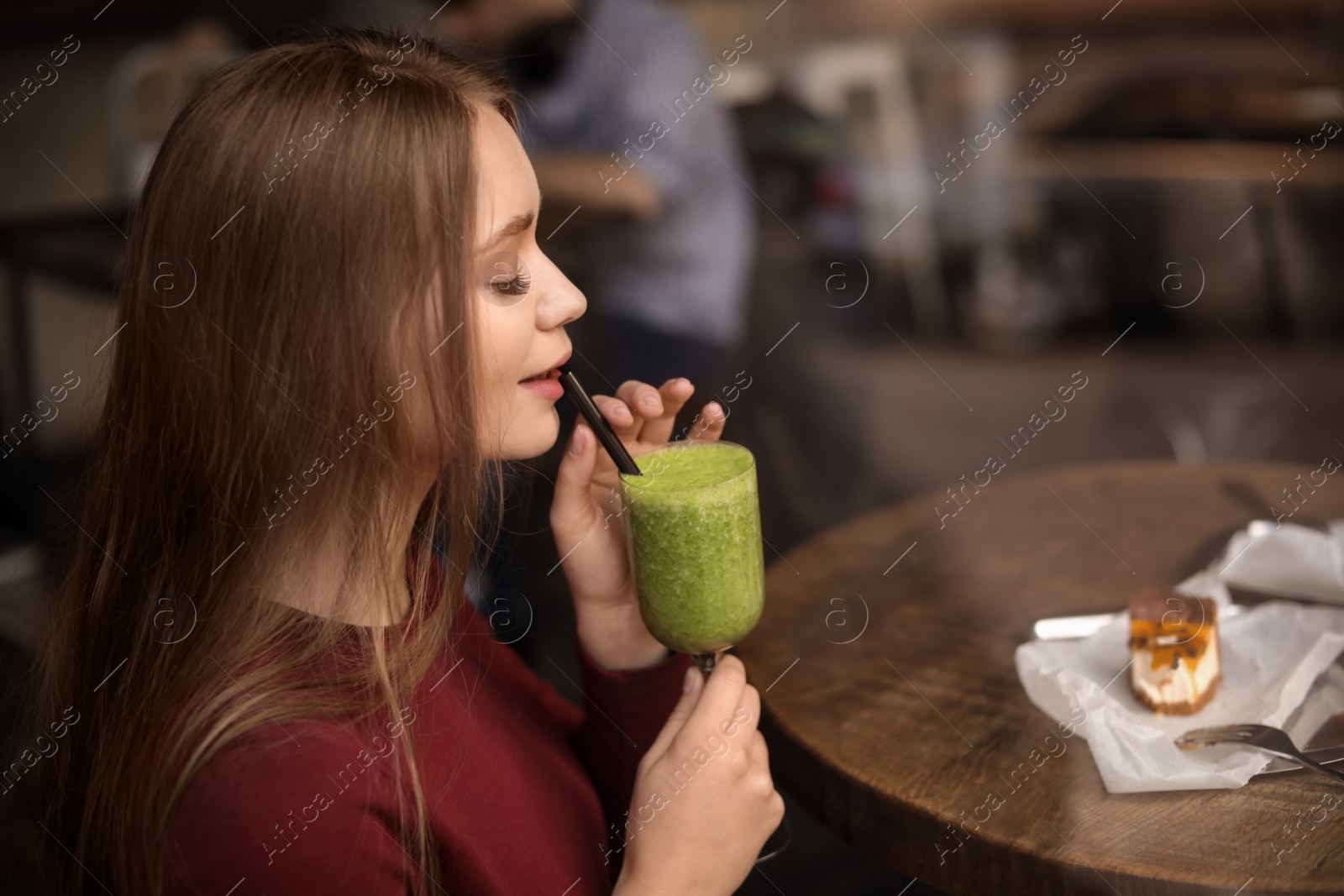 Photo of Pretty young woman with cocktail and cake at table in cafe, view from outdoors through window