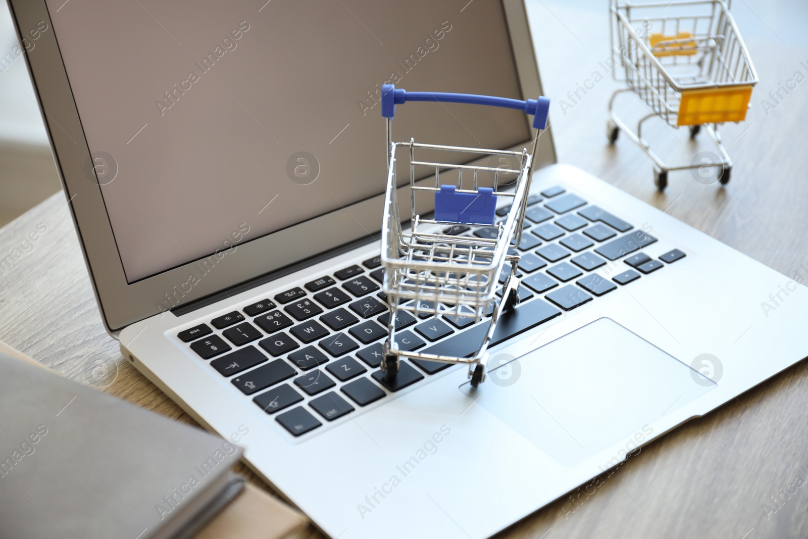 Photo of Internet shopping. Laptop and small carts on table, closeup