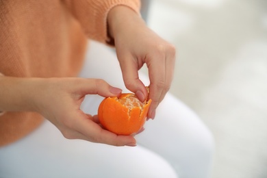 Young woman peeling fresh tangerine on light background, closeup