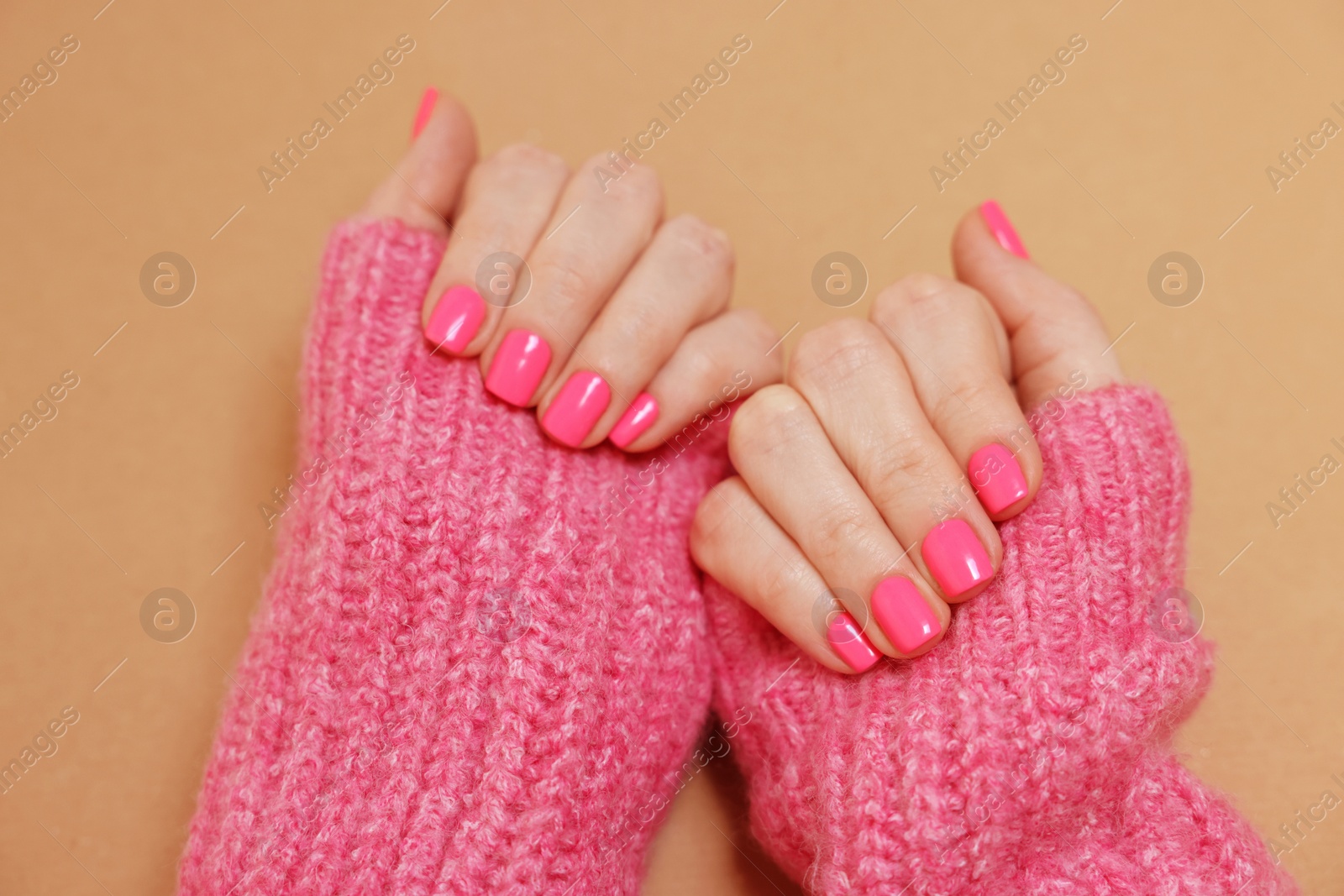 Photo of Woman showing her manicured hands with pink nail polish on dark beige background, closeup