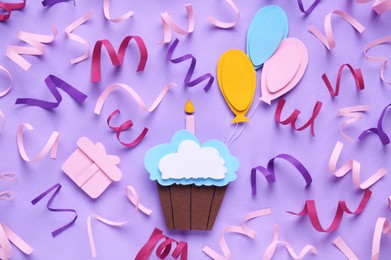 Photo of Birthday party. Paper cupcake, air balloons and confetti on light purple background, flat lay