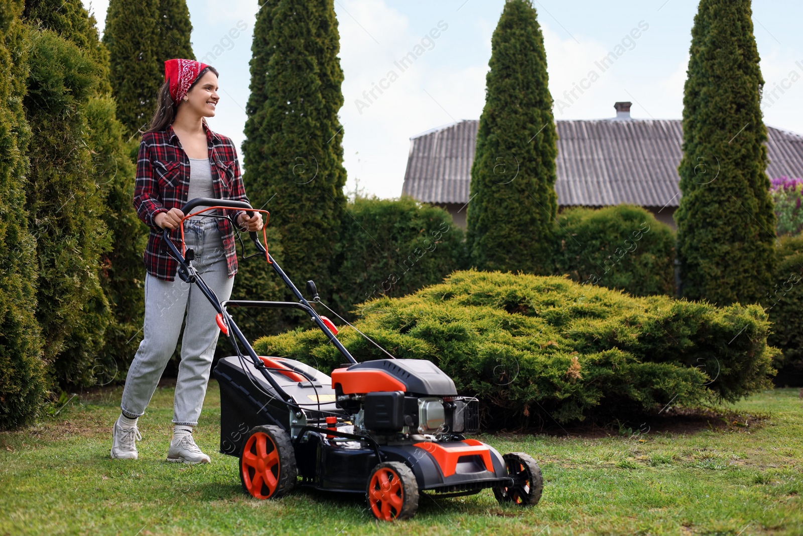 Photo of Smiling woman cutting green grass with lawn mower in garden