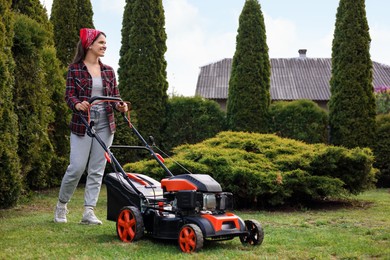 Smiling woman cutting green grass with lawn mower in garden