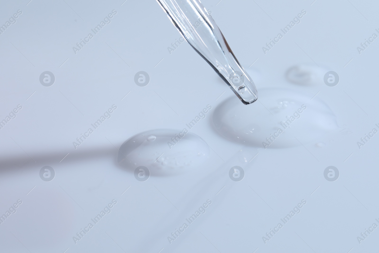 Photo of Glass pipette and transparent liquid on white background, closeup