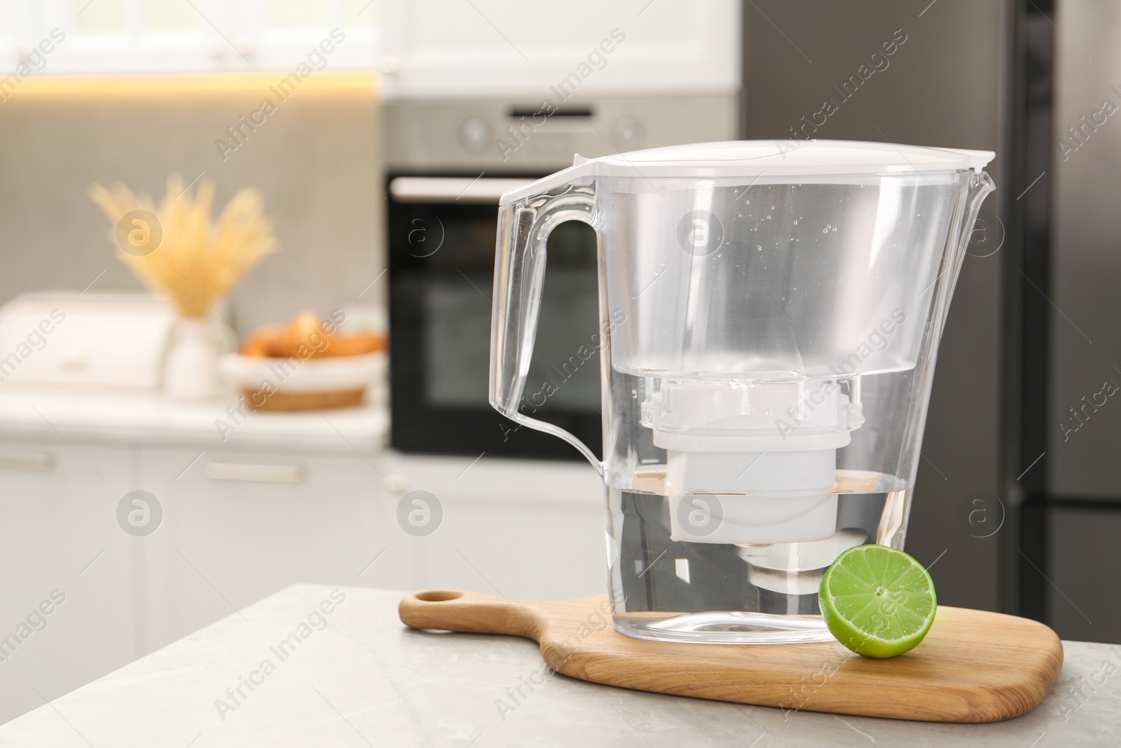 Photo of Water filter jug and lime on light table in kitchen, closeup. Space for text