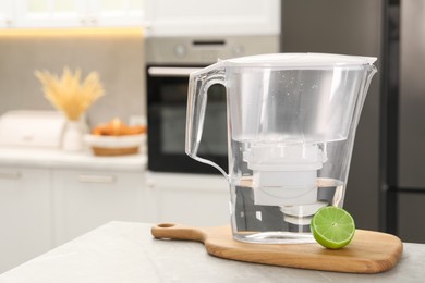 Water filter jug and lime on light table in kitchen, closeup. Space for text