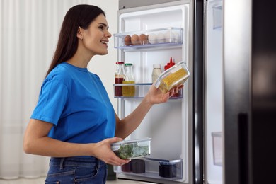 Photo of Young woman taking containers with vegetables out of refrigerator indoors