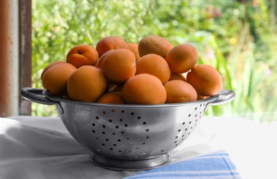 Photo of Colander with delicious ripe apricots on table near window