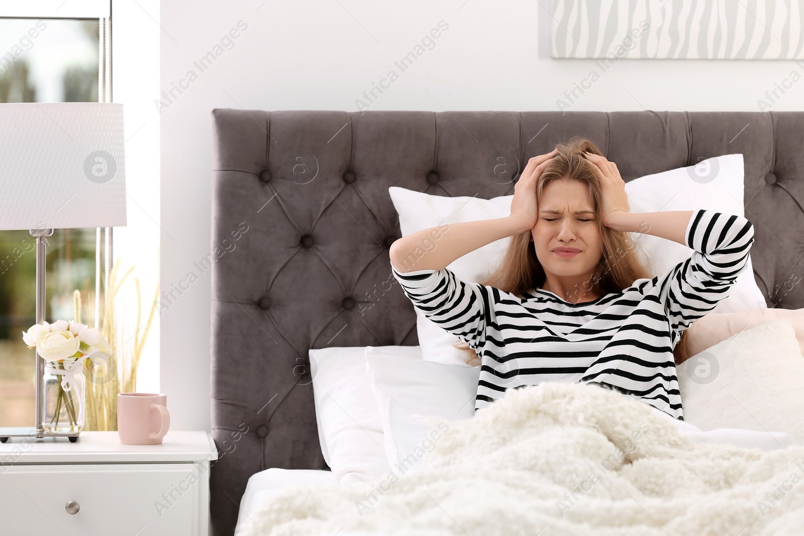 Photo of Young woman suffering from headache in bed with pillows at home