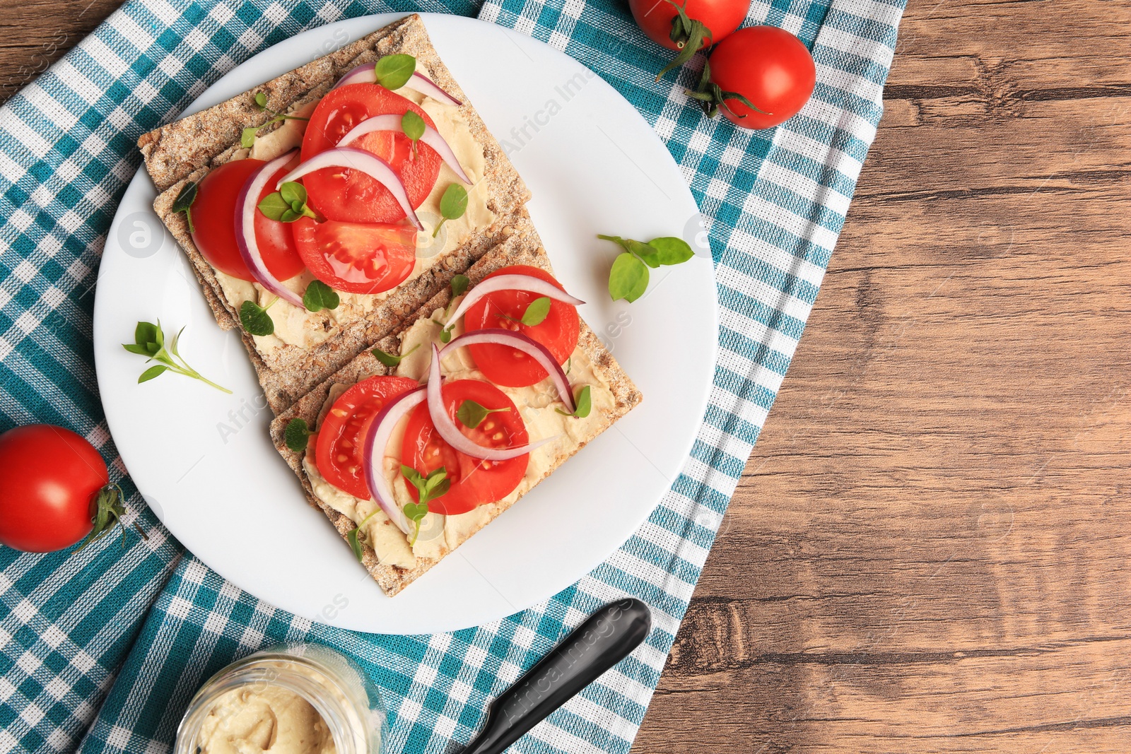 Photo of Fresh crunchy crispbreads with pate, tomatoes, red onion and greens on wooden table, flat lay. Space for text