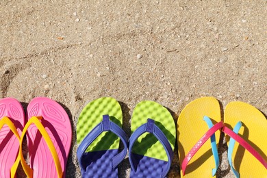 Many different flip flops on sand, flat lay. Space for text