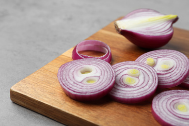 Photo of Cut red onion and wooden board on light grey table, closeup