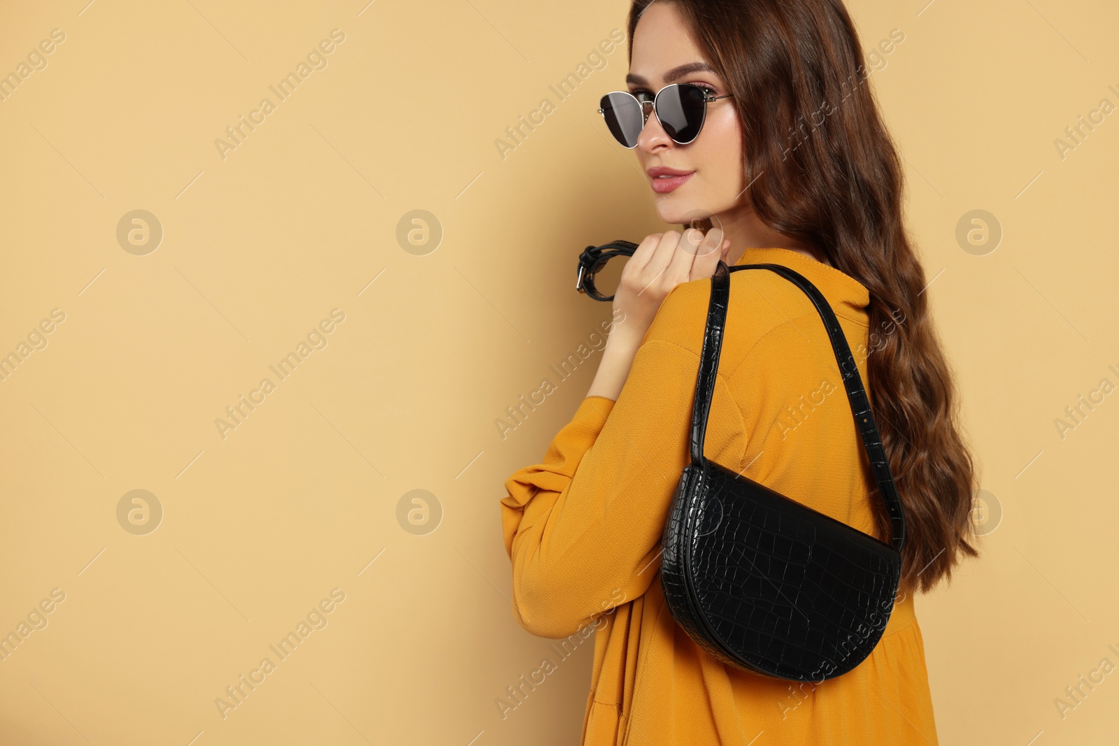 Photo of Beautiful young woman in fashionable outfit with stylish bag on beige background, space for text