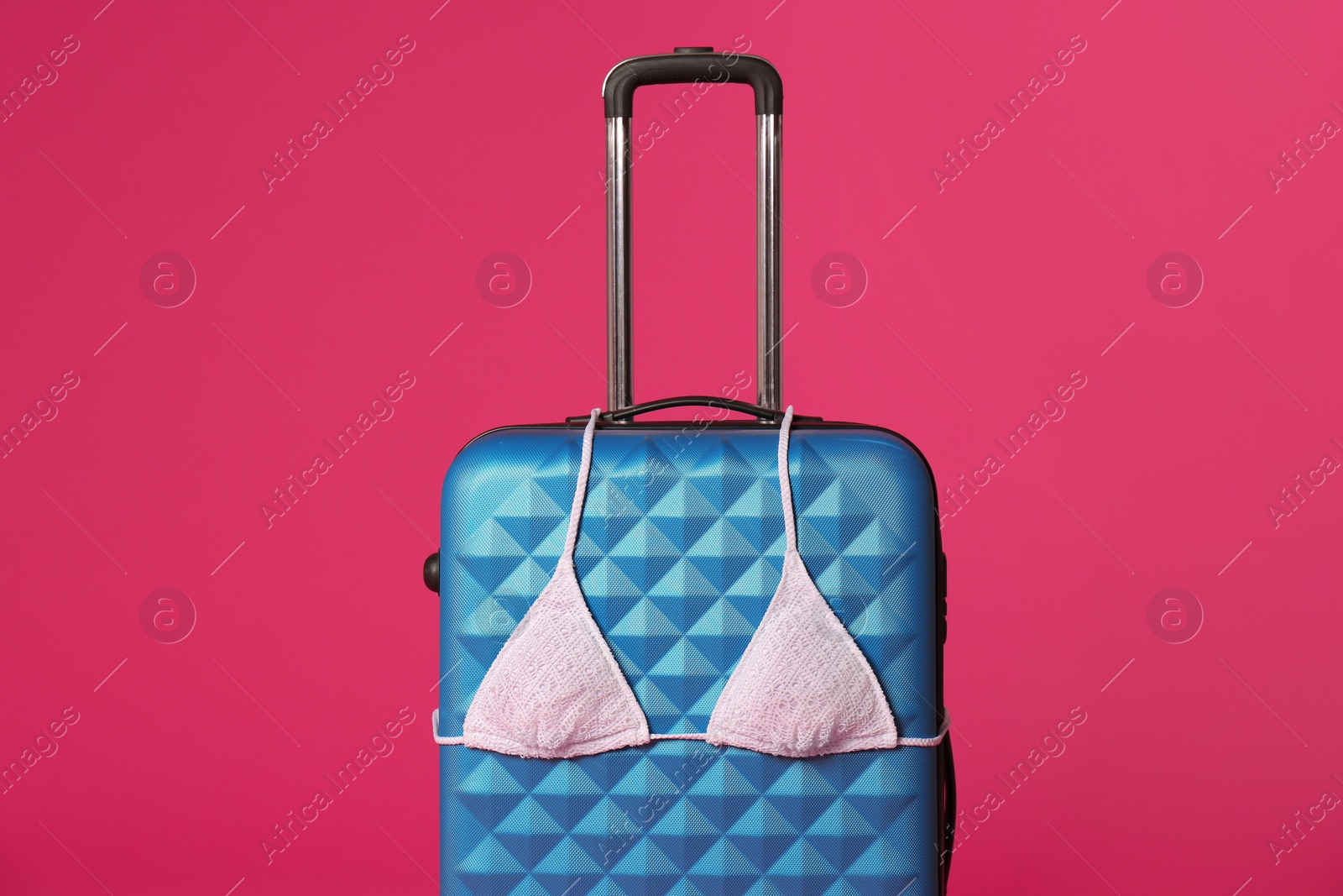 Photo of Stylish suitcase with bikini top on color background