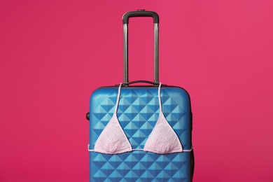 Photo of Stylish suitcase with bikini top on color background
