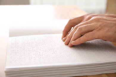 Photo of Blind man reading book written in Braille at table, closeup
