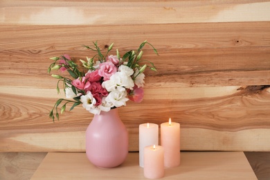 Photo of Burning candles and vase with flowers on table against wooden wall