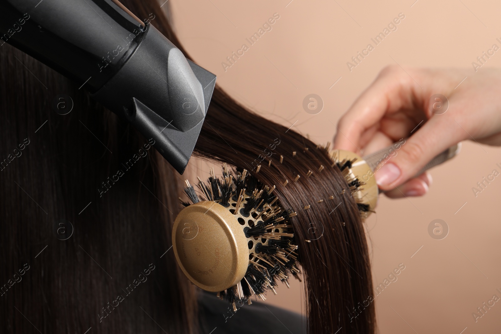 Photo of Hairdresser blow drying client's hair on beige background, closeup