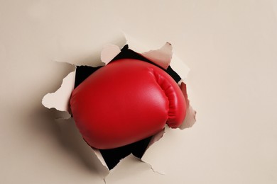 Photo of Man breaking through beige paper with boxing glove, closeup