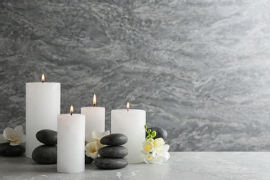 Photo of Composition of burning candles, spa stones and flowers on table. Space for text