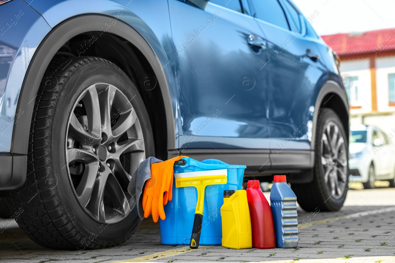 Photo of Car cleaning products and bucket near automobile outdoors on sunny day