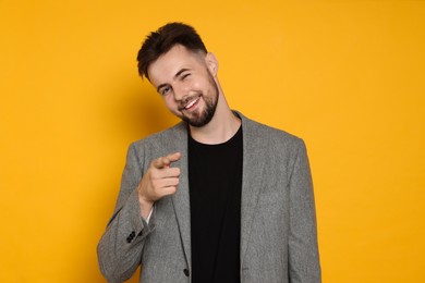 Handsome man in stylish grey jacket pointing at something on yellow background