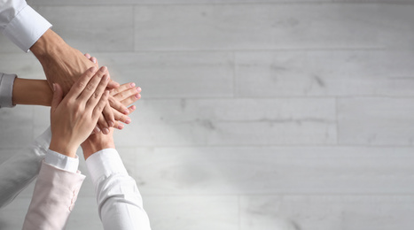 Photo of People holding hands together over light wooden background, top view with space for text. Unity concept