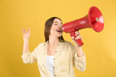 Young woman with megaphone on yellow background