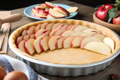 Photo of Dish with fresh apple slices and raw dough on wooden table. Baking pie