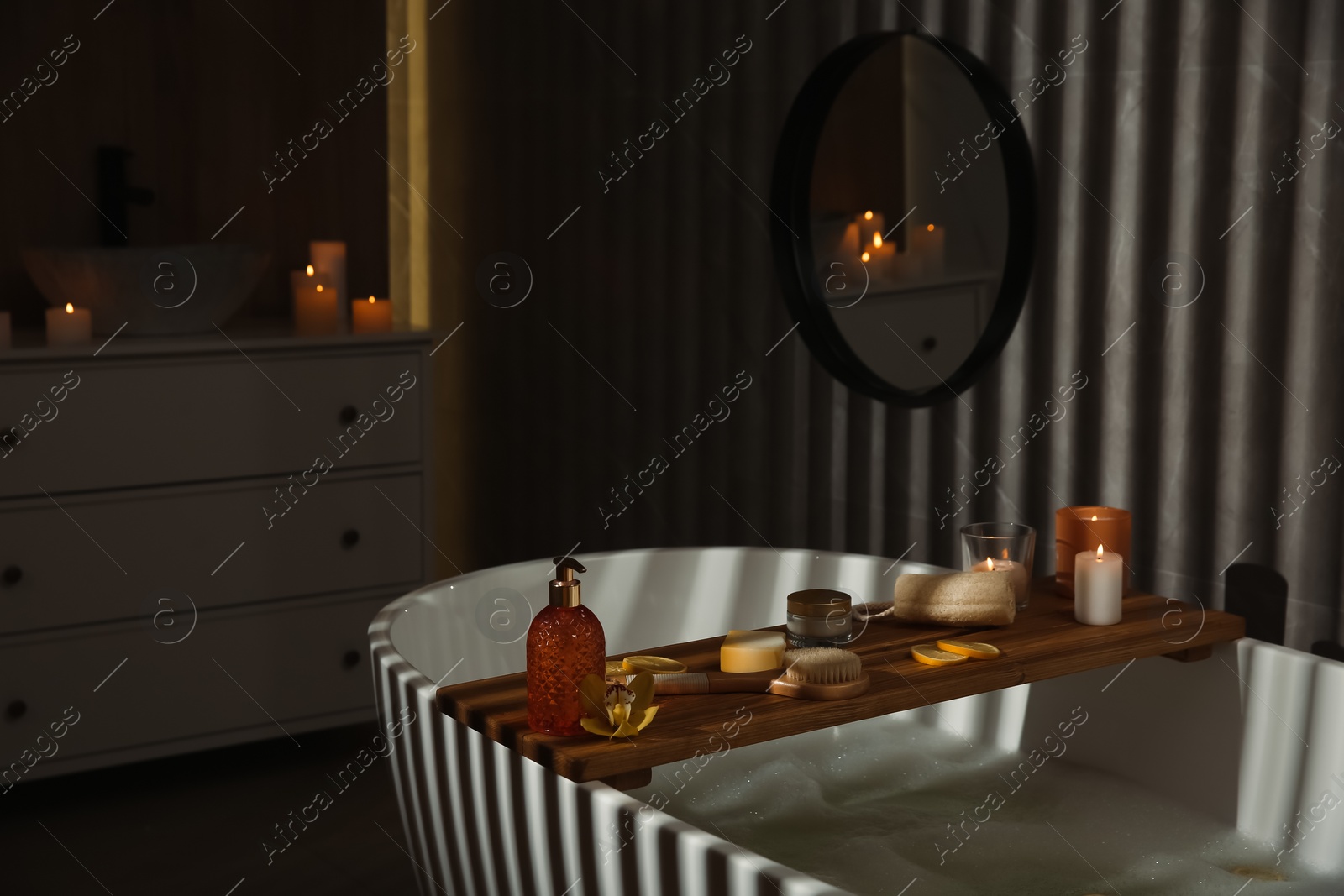 Photo of Wooden bath tray with candles and bathroom amenities on tub indoors