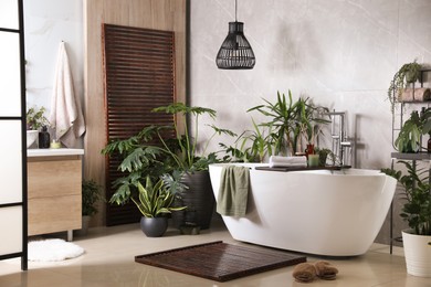 Photo of Modern white tub and beautiful green houseplants in bathroom. Interior design