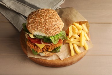 Photo of Delicious burger with crispy chicken patty and french fries on wooden table