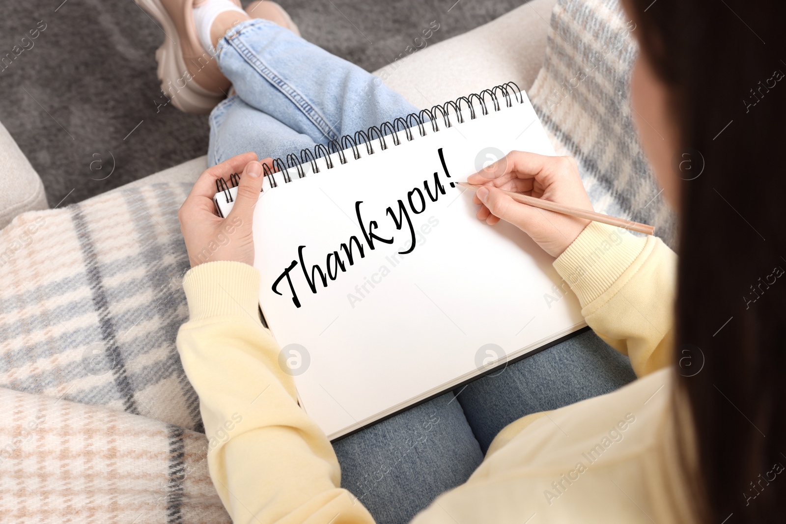 Image of Woman writing phrase Thank You in notebook at home, closeup