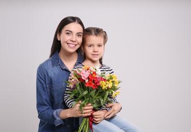 Photo of Happy woman with her cute daughter and bouquet of beautiful flowers on light grey background, space for text. Mother's day celebration