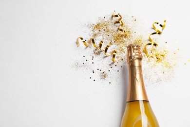 Bottle of champagne with gold glitter, confetti and space for text on white background, top view. Hilarious celebration