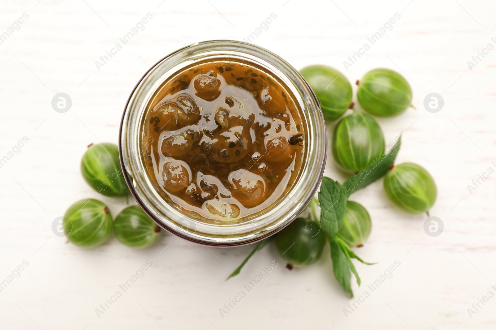 Photo of Jar of delicious gooseberry jam and fresh berries on white wooden table, flat lay