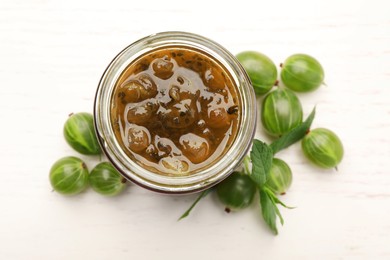 Jar of delicious gooseberry jam and fresh berries on white wooden table, flat lay