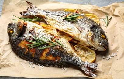 Photo of Delicious roasted fish with lemon on parchment paper, closeup