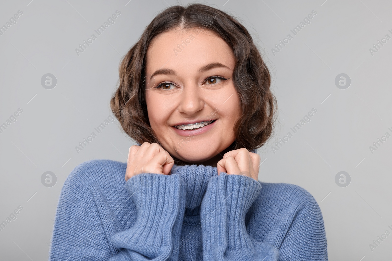 Photo of Smiling woman with dental braces in warm sweater on grey background