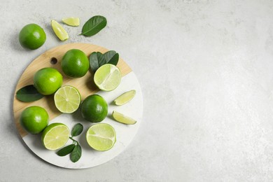 Photo of Fresh ripe limes and leaves on light table, top view. Space for text