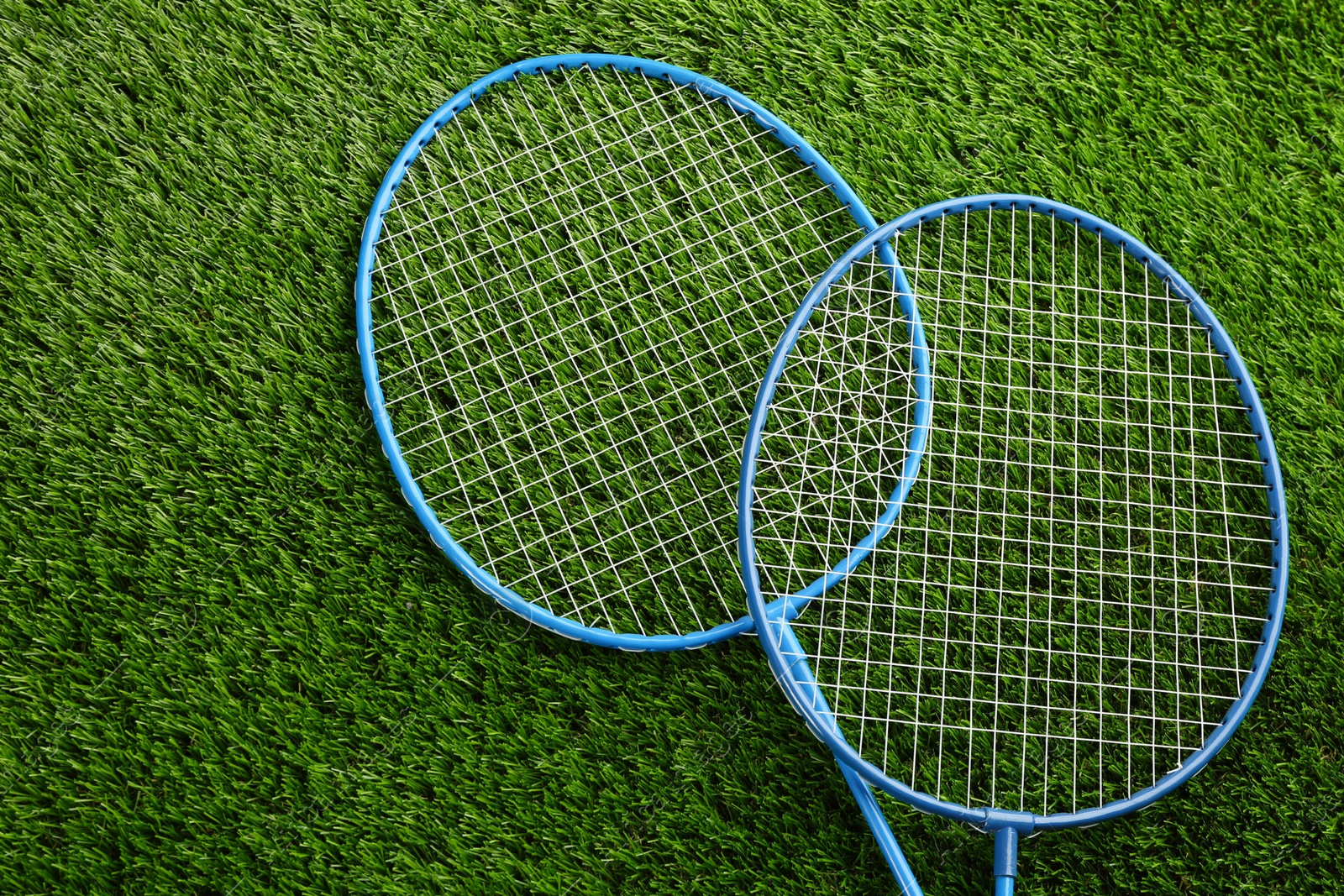 Photo of Badminton rackets on green grass outdoors, above view. Space for text