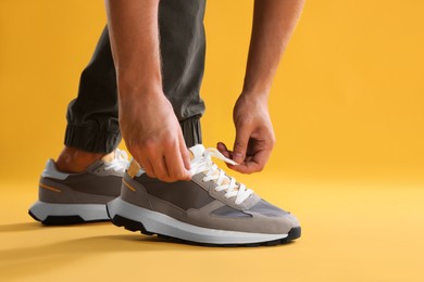 Man tying shoelace of sneaker on yellow background, closeup