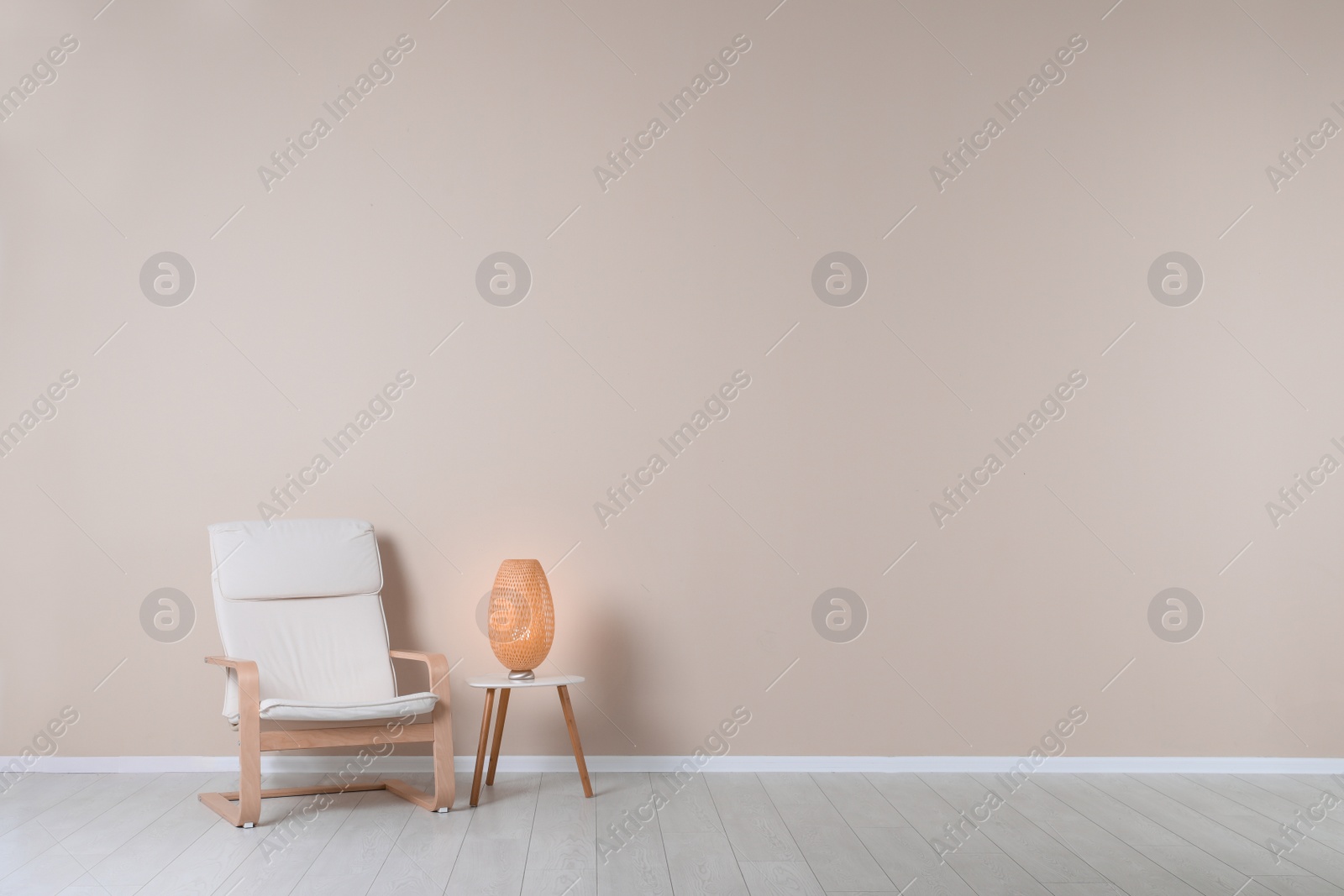 Photo of Comfortable armchair and lamp on table near color wall with space for text. Interior element