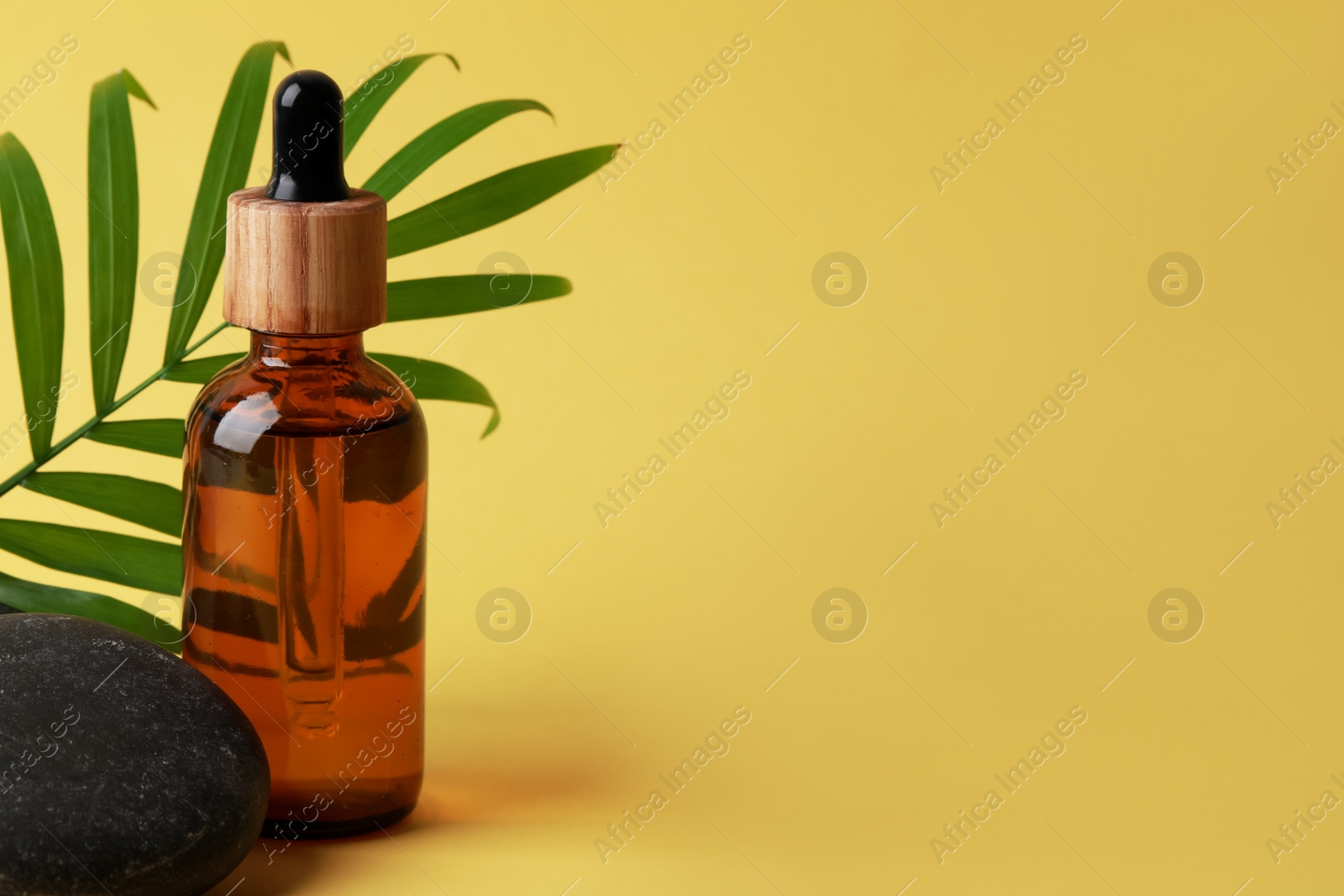 Photo of Bottle of face serum, spa stones and leaf on yellow background. Space for text