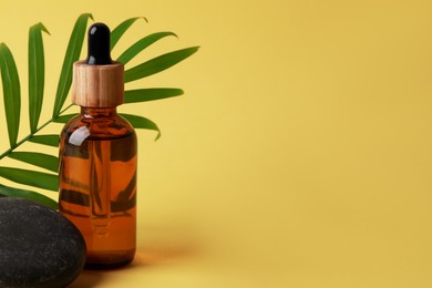 Photo of Bottle of face serum, spa stones and leaf on yellow background. Space for text