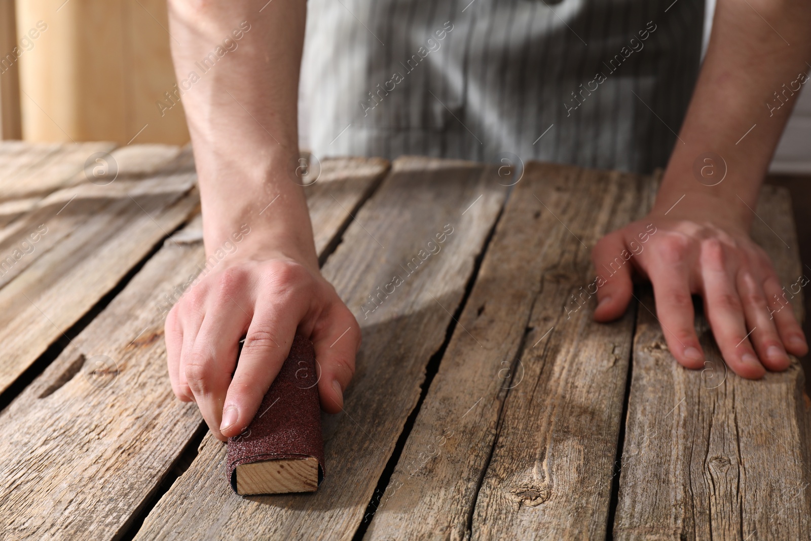 Photo of Man polishing wooden table with sandpaper indoors, closeup