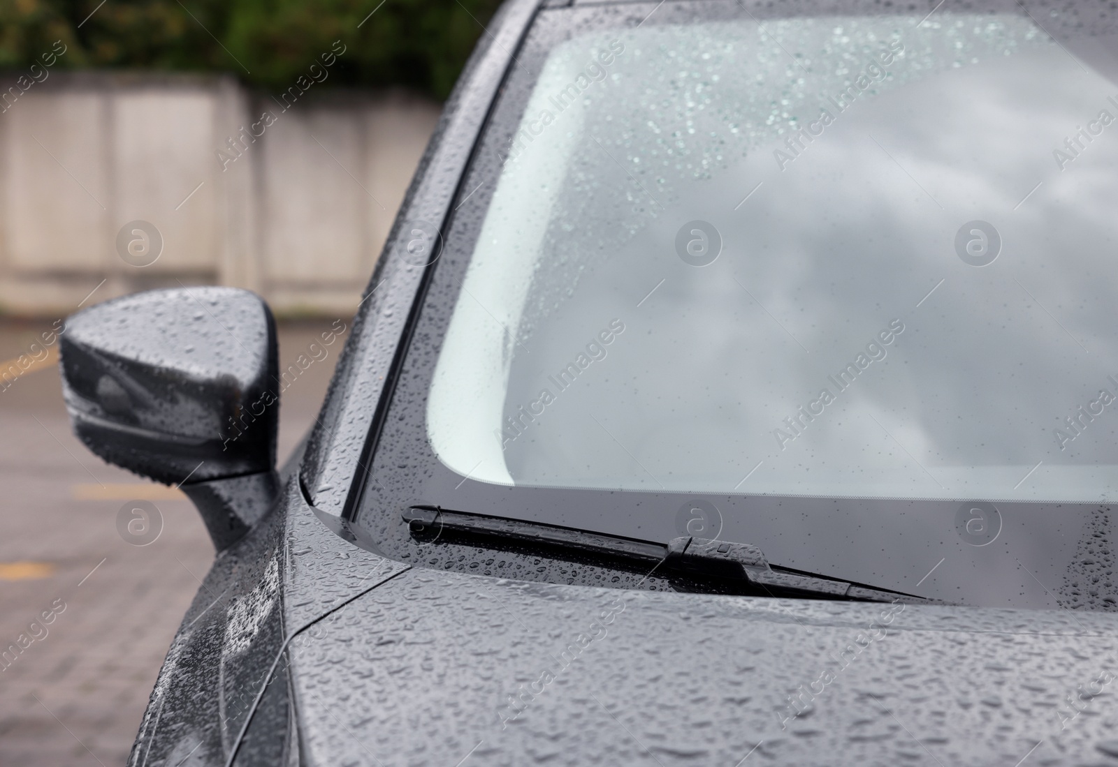 Photo of Car wiper cleaning water drops from windshield glass outdoors, closeup