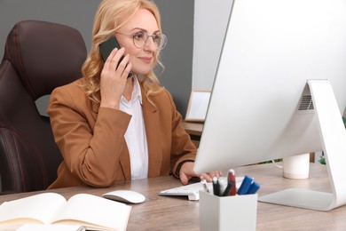 Photo of Lady boss talking on smartphone near computer at desk in office. Successful businesswoman