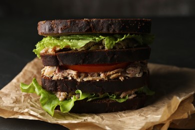 Delicious sandwich with tuna, tomatoes and lettuce on black table, closeup