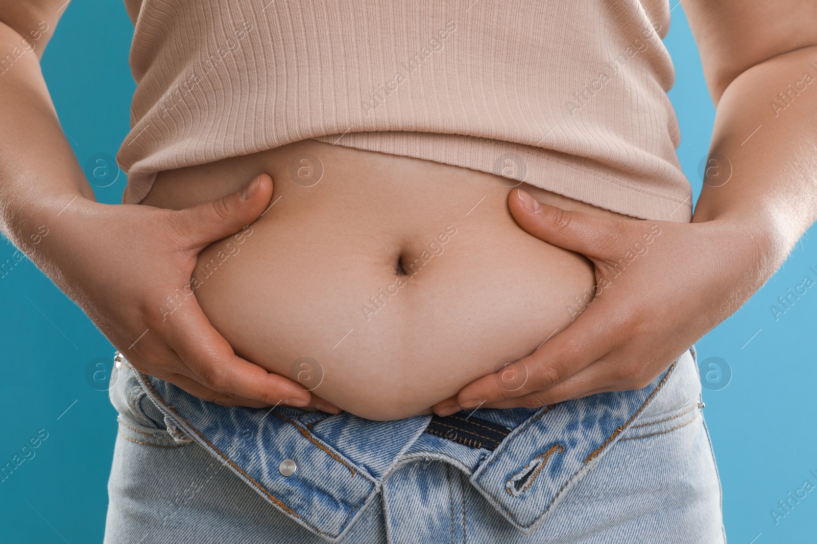 Photo of Woman touching belly fat on light blue background, closeup. Overweight problem